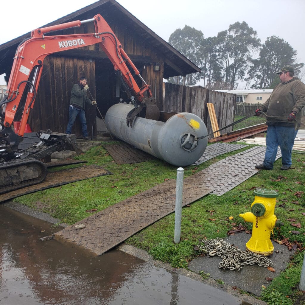 Men Working With Backhoe To Move Water Tank